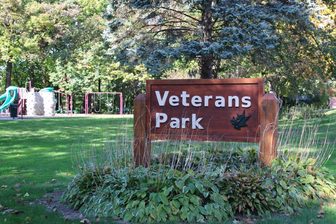 The Veterans Park sign in Appleton, with playground equipment and trees behind it