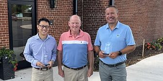 Three men holding awards outside a brick building in Wausau