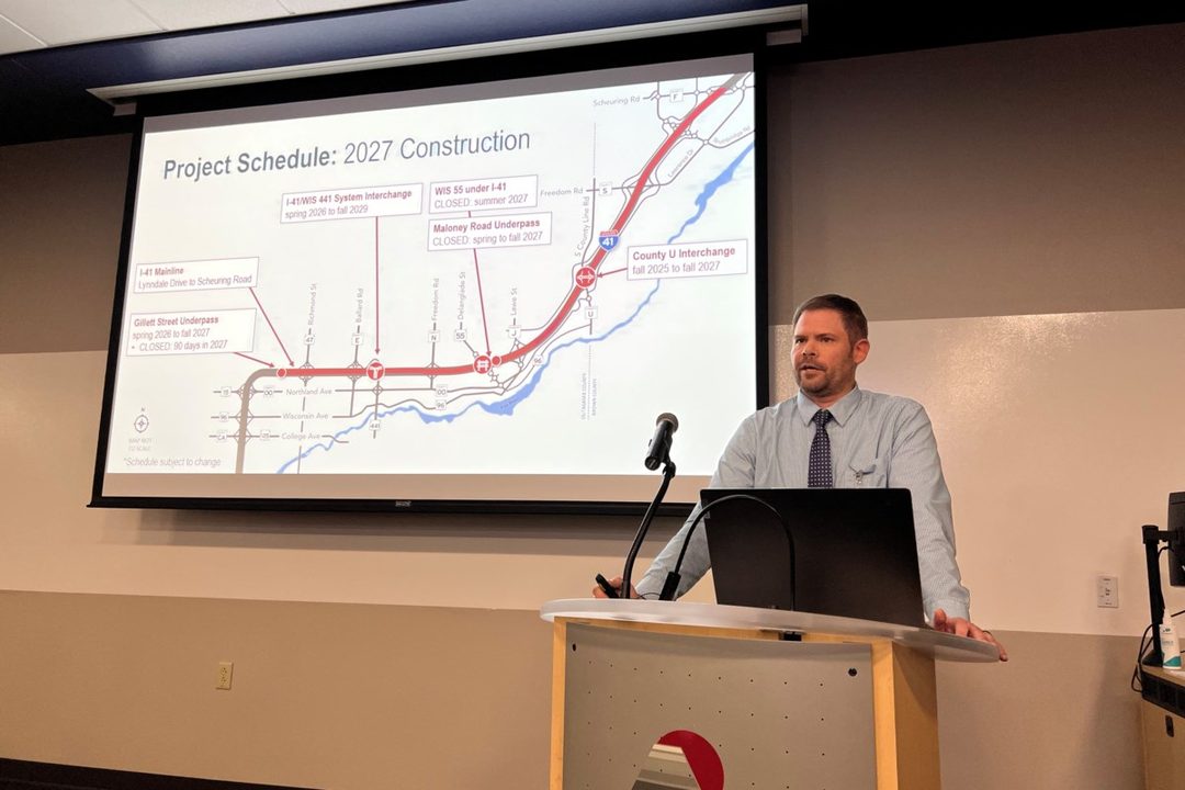 A Wisconsin DOT presenter at a podium in front of an I-41 project schedule map at Fox Valley Technical College