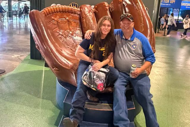 Leah and Dirk MacDonald sitting in the giant Brewers baseball glove at American Family Field