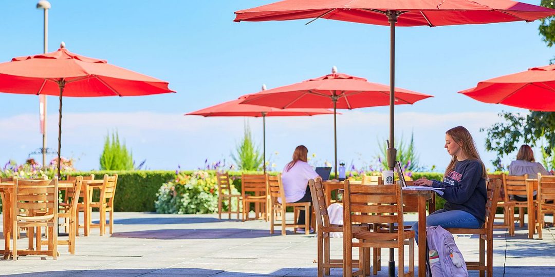 Students studying at outdoor tables under red umbrellas on the Carthage College campus in Kenosha