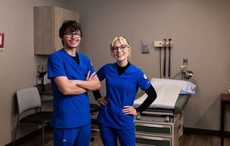 Two medical assistant students in blue scrubs in an exam room at Northwood Technical College