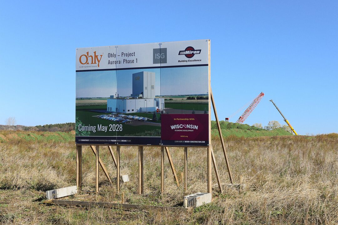Project sign for Ohly's Project Aurora Phase 1 at the Eau Claire construction site, with cranes in the background