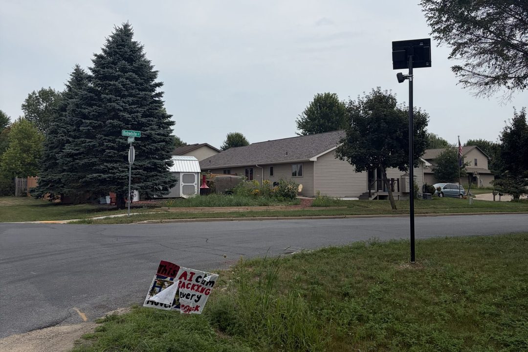 A Flock camera in River Falls, with a sign below it criticizing the cameras for tracking