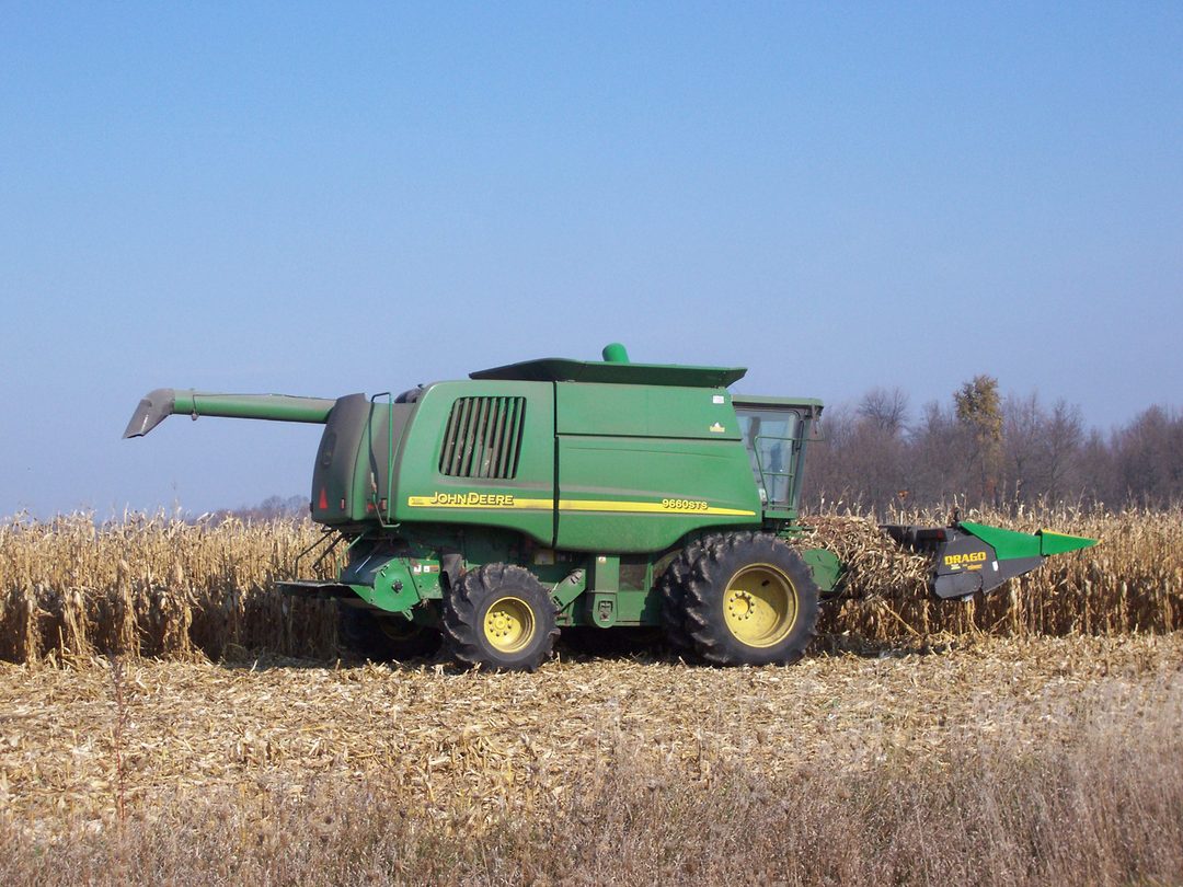 A John Deere combine harvester working in a corn field